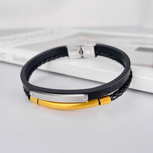 Détail du bracelet en cuir tressé noir avec tube doré et fermoir en acier inoxydable argenté