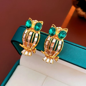 Macro shot of owl earrings with green gem eyes on dark green jewelry box