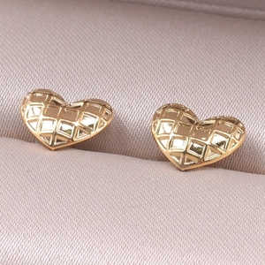 Detailed macro view of gold heart stud earrings with engraved grid pattern on a jewelry box