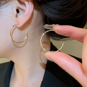 Gros plan de grandes boucles d'oreilles clips dorées montrant la fine texture métallique