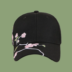Detailed embroidery of pink plum blossoms on a black cotton baseball cap surface