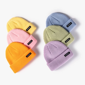 Candy colored knitted beanies in ribbed texture with letter patches on white background