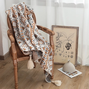 Bohemian geometric knit blanket with tassels draped over a vintage wooden armchair