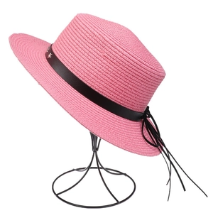 Detail of pink straw sun hat with black decorative band and star-shaped metal buckle