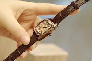 Macro shot of rose gold tonneau watch face with crystal bezel and brown leather strap