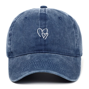 Dettaglio del ricamo a cuore bianco su cappellino in denim di cotone lavato blu