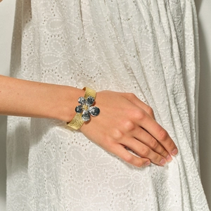 Detail of a 18k gold plated stainless steel cuff bracelet with a textured daisy flower charm