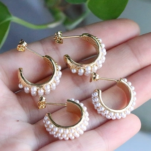 Detail view of C-shaped golden earrings with triple rows of inlaid pearls on a hand