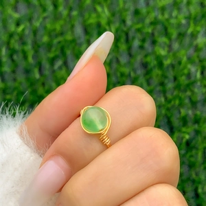 Macro shot of handmade gold wire-wrapped ring featuring a green stone on a finger