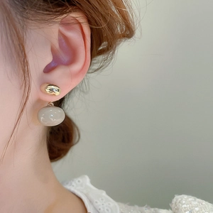 Vue détaillée de boucles d'oreilles dorées avec pendentif ovale blanc sur un mannequin