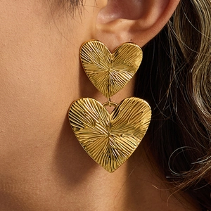 Macro shot of gold textured double heart earrings worn by a model showing luxury finish