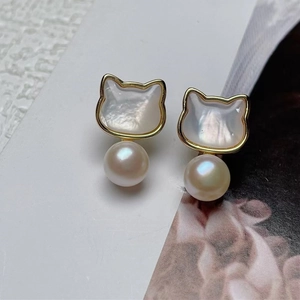 Macro shot of cat-shaped gold earrings with iridescent shell inlay and white pearls