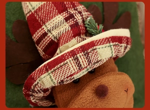 Close-up of plush reindeer head wearing a festive red and green plaid fabric hat