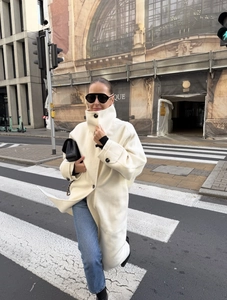 Close-up of white cashmere blend long coat with decorative black buttons in urban street setting