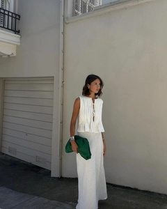Detail of white pleated sleeveless top and long skirt with green woven clutch bag