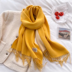 Detailed shot of a yellow cashmere-feel scarf with fringe tassels and a woven label