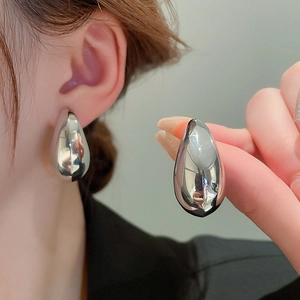 Macro shot of high-polish metallic waterdrop earrings worn on ear showing glossy finish