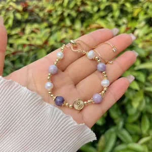 Macro shot of 18k gold beads with purple stones and a Virgin Mary charm on an adjustable band