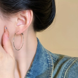 Side view of model wearing large silver twist hoop earrings in a minimalist style