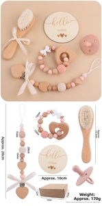 Detailed set of wooden baby teether, soft brush, and pink silicone pacifier clip in a gift box