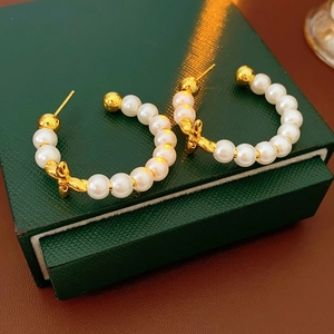 Close-up of 18K gold plated pearl earrings with bow detail on a velvet jewelry box