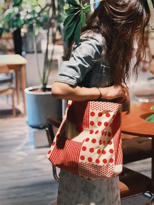Sac fourre-tout en toile à pois rouges et grille porté dans un café chaleureux