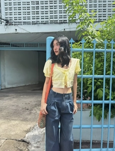 Détail d'un haut jaune à lacets avec manches bouffantes et jean large à taille haute