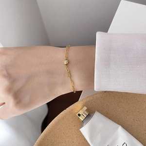 Gold paperclip chain bracelet with a bezel-set round diamond on a model's wrist