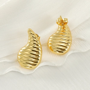 Close-up of golden teardrop earrings with textured horizontal ridges on white silk