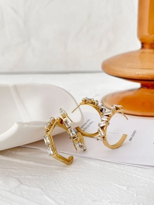 Detailed close-up of golden geometric pentagon and C-shaped earrings with inlaid crystals
