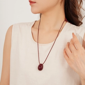 Collier avec pendentif ovale rouge foncé et cordon ethnique porté par un mannequin