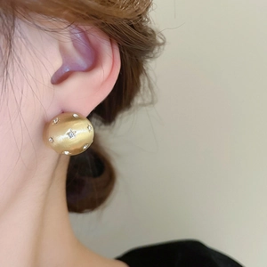 Detailed close-up of matte gold dome earrings with sparkling star-shaped crystals