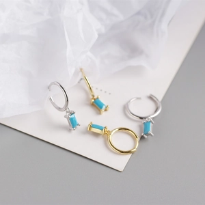 Detail of gold and silver rectangle turquoise charm hoop earrings on a textured paper background