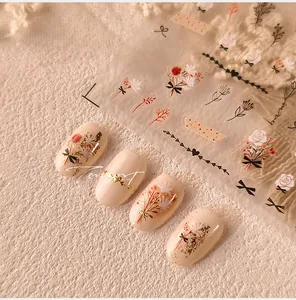 Detail of floral nail stickers with gold foil accents on cream-colored manicured nails