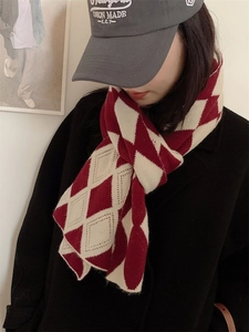 Détail d'une écharpe en maille à losanges rouge et beige avec une casquette brodée