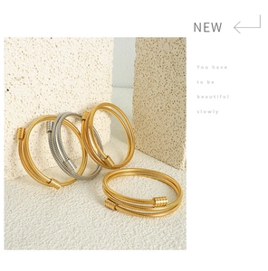 Detail of layered gold and silver snake texture bracelets on a beige stone surface