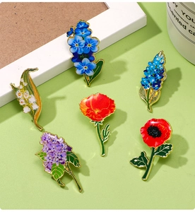 Flat lay of six colorful enamel floral brooches featuring lilies and poppies on a green desk