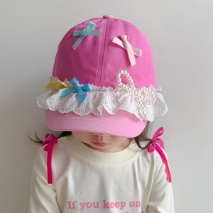 Pink children's baseball cap with white lace, silk bows and pearls on a young girl