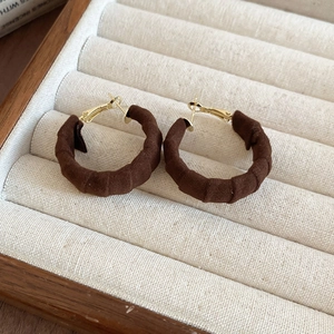 Detailed view of dark brown velvet fabric hoop earrings on a beige jewelry display tray