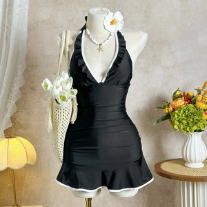 Detail of black halter one-piece swimsuit featuring white ruffle trim and ruched waist design