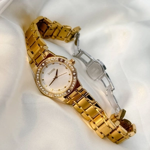 Elegant gold luxury women's watch with crystal bezel on white silk fabric background