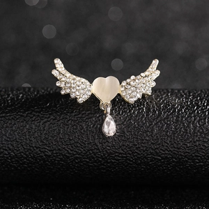 Detailed view of heart-winged gold brooch with white rhinestones and opalescent stone