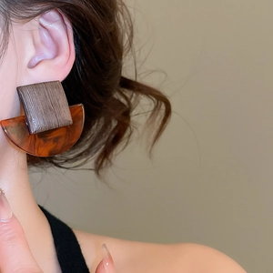 Close-up of geometric resin and wood earrings worn by a model in warm brown tones