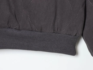 Detail of dark gray diamond quilted fabric with elastic ribbed hem on a bomber jacket