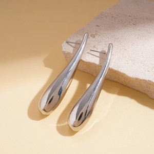 Macro shot of silver teardrop earrings resting on a textured beige stone base