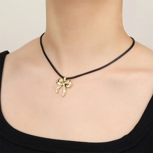 Close-up of 18k gold stainless steel bow pendant worn on a black wax cord necklace