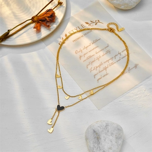 Elegant gold double-layered heart necklace with black pendant on white textured background