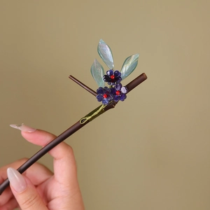 Detail of dark bamboo hair stick with purple flowers and iridescent green leaves