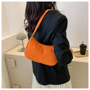 Orange corduroy baguette bag worn over the shoulder with black blazer and white skirt