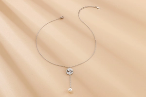 Detail of silver pearl necklace with LOVE lettering on round pendant and tassel drop